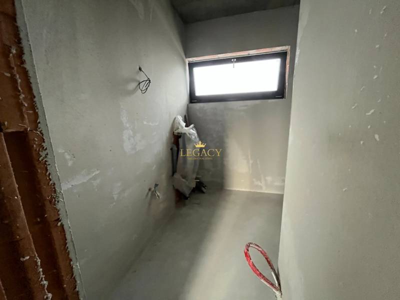 An unfinished room in a family house with a window and exposed piping.