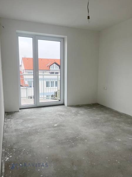An empty room with a gray floor and a large window in a three-room apartment.