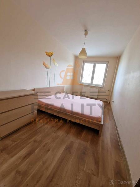 A bedroom in a two-room apartment with a wooden decor floor and a floral motif on the wall.