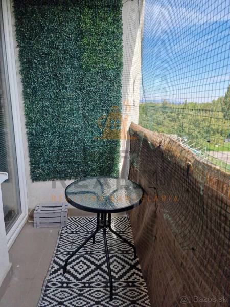 Balcony of a 2-room apartment with a round table, carpet, and green vertical wall.