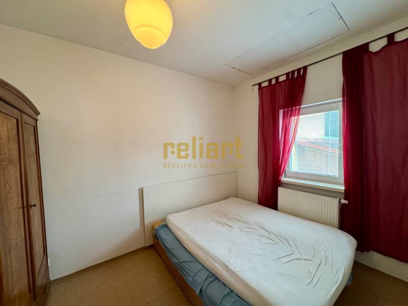 Bedroom in a 2-room apartment with a wooden wardrobe and a window with red curtains.