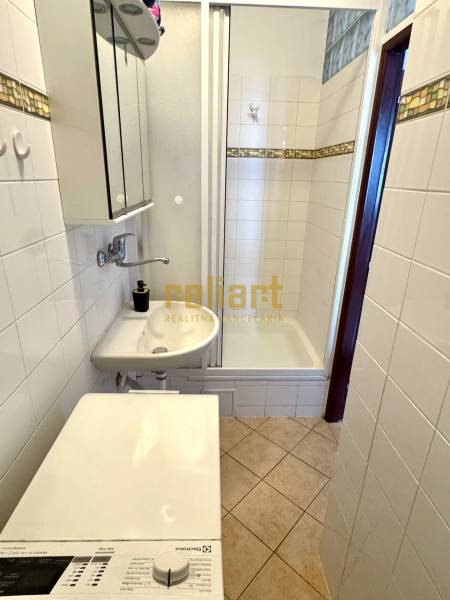 Bathroom in a 2-room apartment with a washing machine, sink, and shower. Tiled floor.