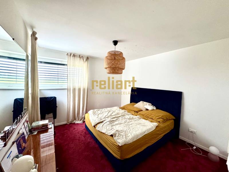A bedroom in a family house with a red carpet, a blue bed, and a large window.