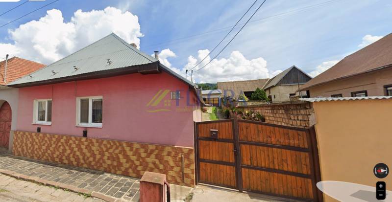 A family house in Jelšava with a pink facade, a sloped roof, and a wooden gate.