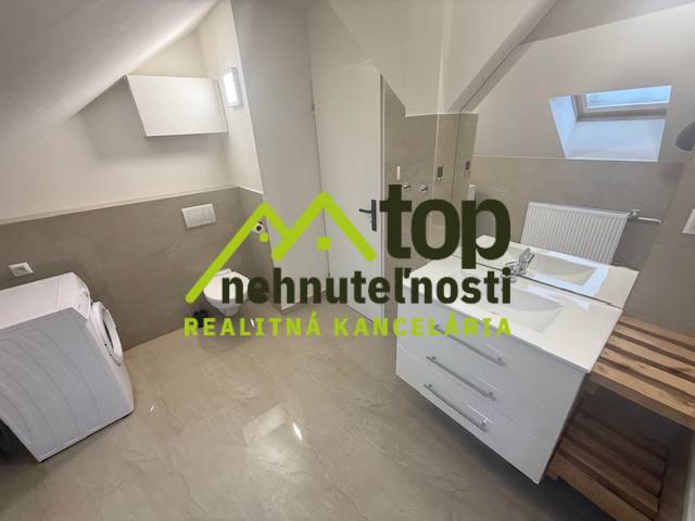 Attic bathroom of a studio apartment with a washing machine and a sink, wooden decor flooring.