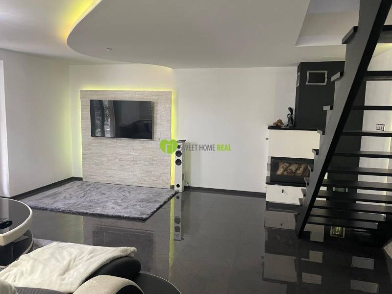 Living room in a family house with a staircase, fireplace, and television on the wall.