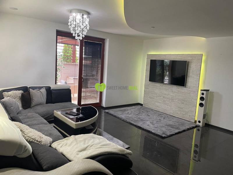 Living room in a family house with a sofa and a television on a wall with stone cladding.