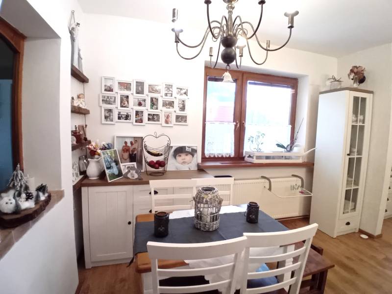 A dining room in a family house with white furniture, pictures on the wall, and a decorative chandelier.