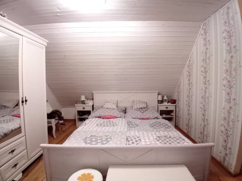 Attic bedroom in a family house with floral wallpaper and wood-patterned flooring.
