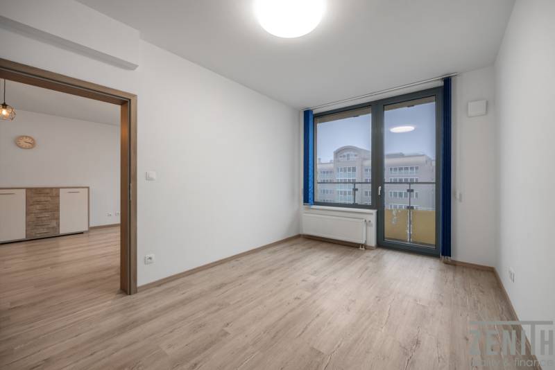 A room with a wooden decor floor, a window, and glass doors in a two-room apartment.