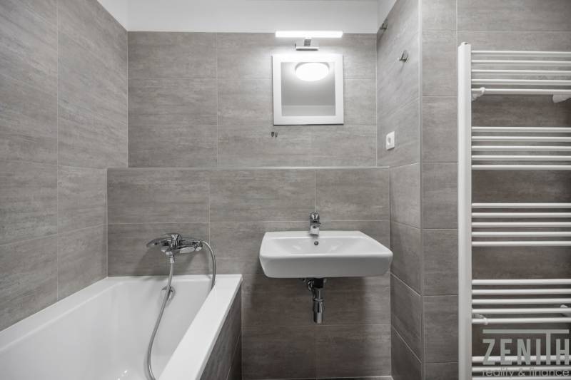 Bathroom of a 2-room apartment with a bathtub, sink, and ladder radiator.