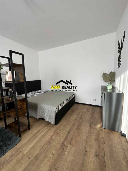 A bedroom in a studio apartment with a wood-patterned floor and minimalist furnishings.