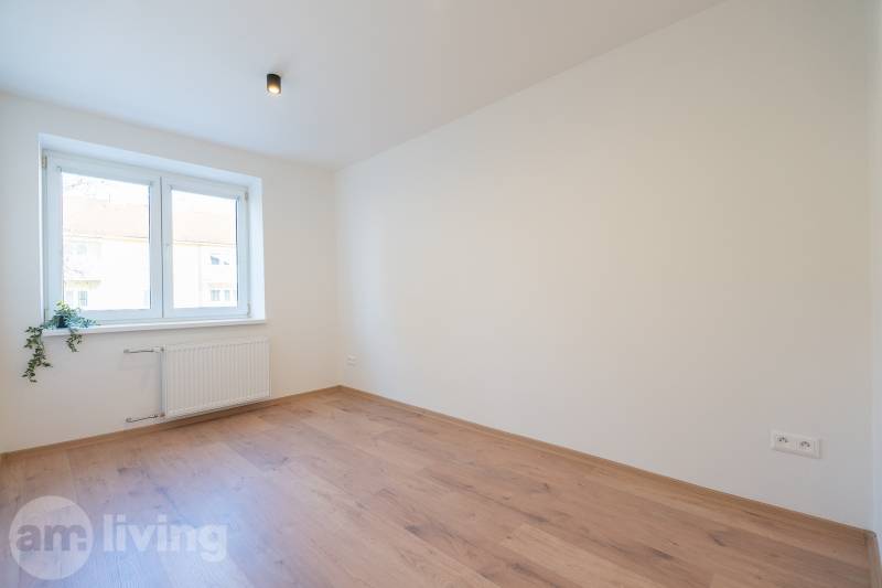 A bright room with a wood-patterned floor in a three-room apartment with a light above the window.