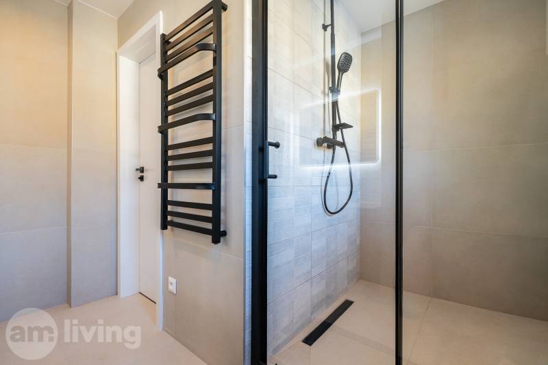 A bathroom with a shower and a black ladder in a 3-room apartment.