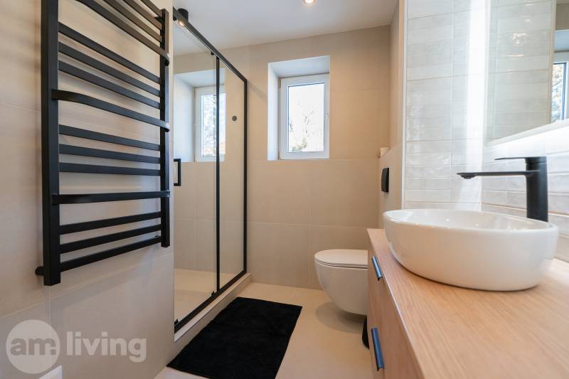 A bathroom in a 3-room apartment with a black ladder radiator and a glass shower enclosure.