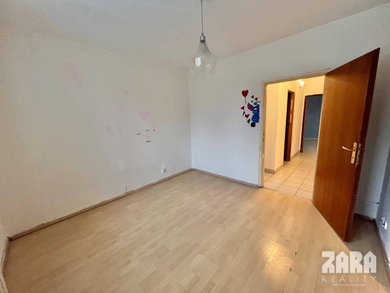 A room with a wooden decor floor in a 3-room apartment, light wall, open door.