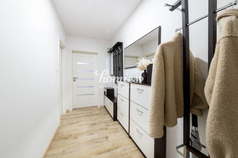 A hallway in a 2-room apartment with a wooden decor floor, a shoe cabinet, and a coat rack.