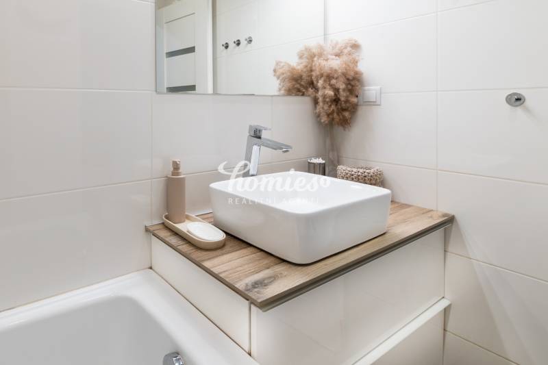 Bathroom in a 2-room apartment with a sink, wooden decor flooring, and decorative plant arrangement.