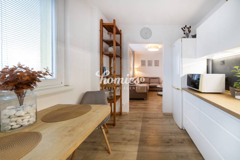 A kitchen in a 2-room apartment with a dining table, a shelf, and a floor with a wood decor.