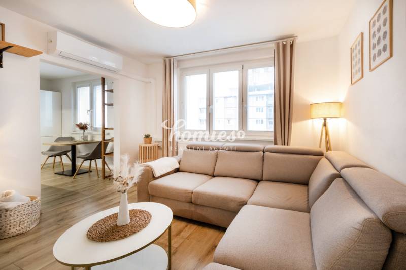 A bright living space in a two-room apartment with a wooden decor floor and a comfortable sofa.