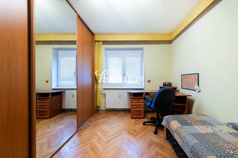 A room with a wood-patterned floor, a table, and a wardrobe in a three-room apartment.