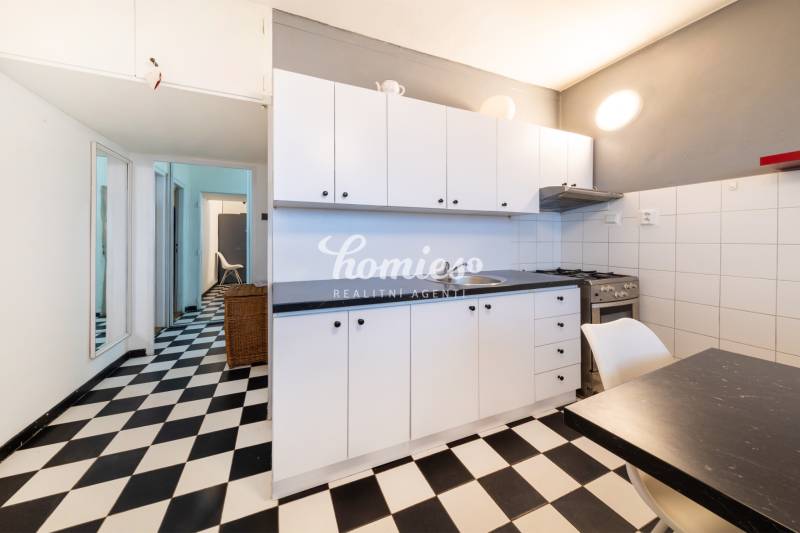 A kitchen in a 3-room apartment with black and white flooring, white cabinets, and a stove.