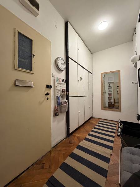 Hallway of a 2-room apartment with a wooden decor floor, storage cabinets, and a runner.