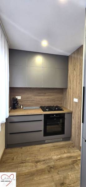 A kitchen in a 3-room apartment with modern appliances and a wooden decor floor.