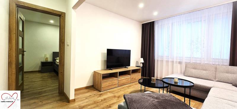 Living room in a 3-room apartment with a wooden decor floor and a large television.