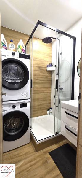 A bathroom in a 3-room apartment with a wooden decor floor, a shower corner, and a washing machine.