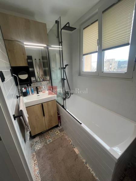 Bathroom in a 4-room apartment with a bathtub, sink, mirror, and colorful tiles.