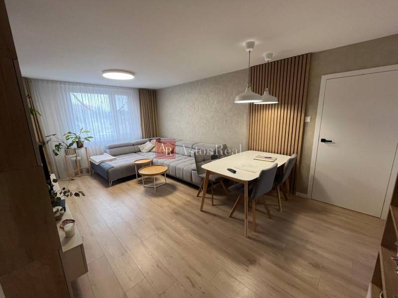 Living room of a 4-room apartment with wood-patterned flooring, a gray sofa, and a dining table.