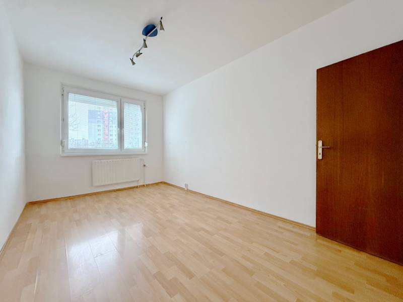An empty room in a 4-room apartment with a wood-patterned floor and a large window.
