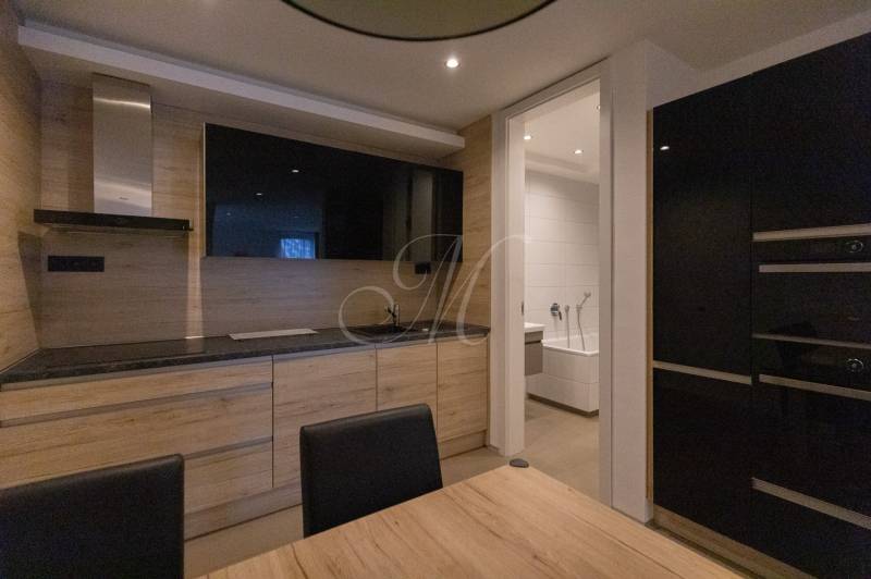 A kitchen in a 2-room apartment with a wood-patterned floor and an installed television.