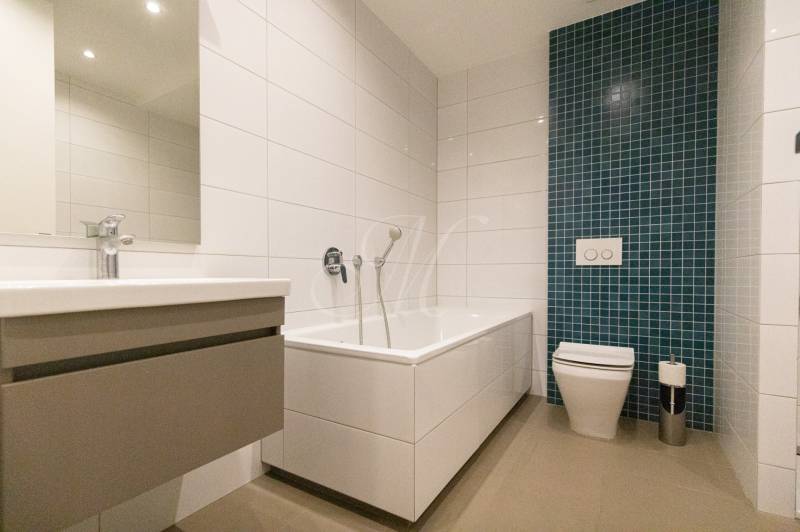 Bathroom in a 2-room apartment with a bathtub, sink, and green tile panel.
