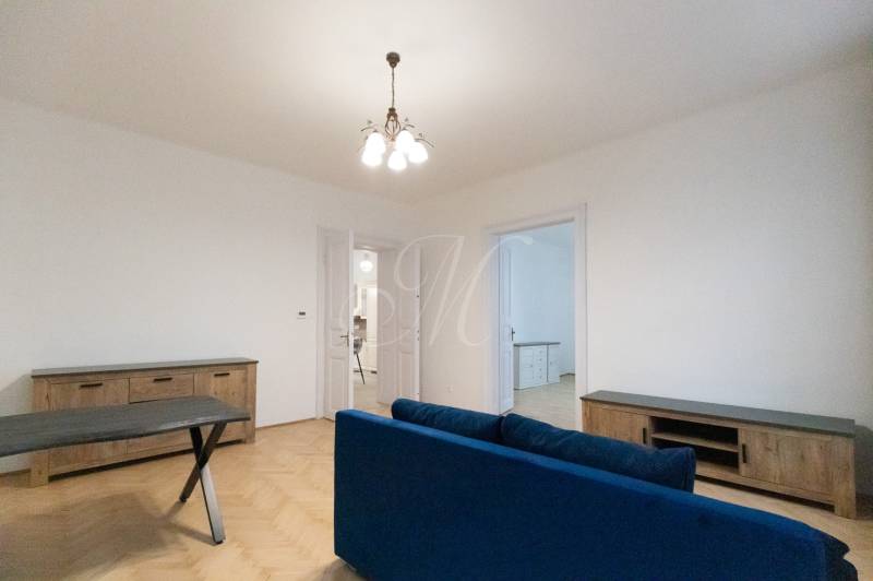 Living room in a three-room apartment with a wooden decor floor and a blue sofa.