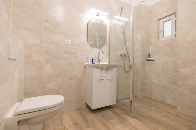 A bathroom with a wooden decor floor, a shower, and a cabinet in a 3-room apartment.