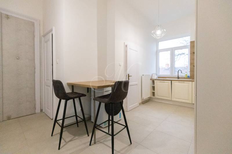 A kitchen in a 3-room apartment with a bar counter, two chairs, and a large window.