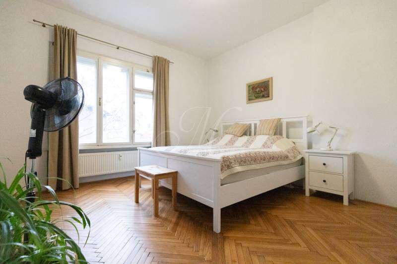 A bedroom with light furniture, a large window, and a floor with a wood decor in a 2-room apartment.