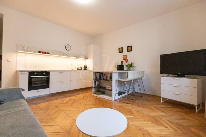 Living room in a two-room apartment with a kitchen, wooden decor flooring, TV, and table.