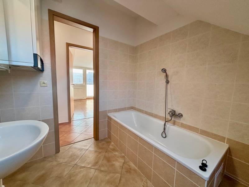 Bathroom with tiles next to a 2-room apartment, bathtub and sink, spacious layout.