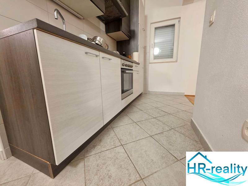 A kitchen in a holiday apartment with tiled flooring and a modern unit with dark cabinets.