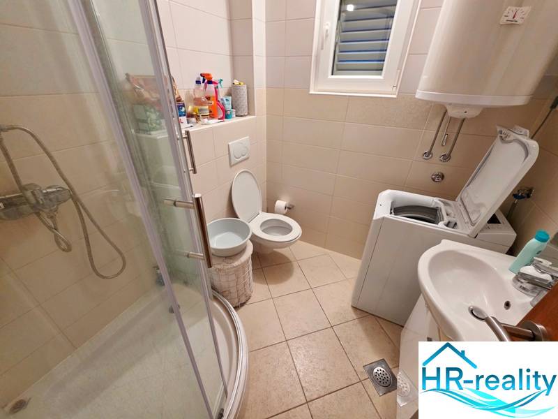 Bathroom in a Holiday Apartment with a toilet, shower, and washing machine.