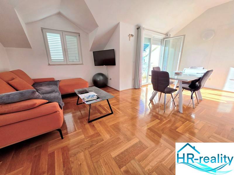 Recreational apartment with an orange sofa, dining table, and wood-patterned flooring.