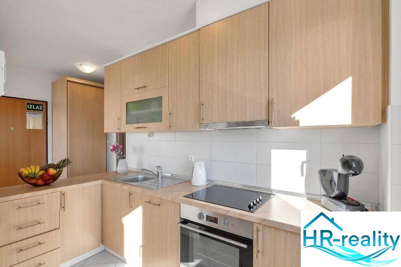 Kitchen area in a 3-room apartment with light wooden cabinets and appliances.