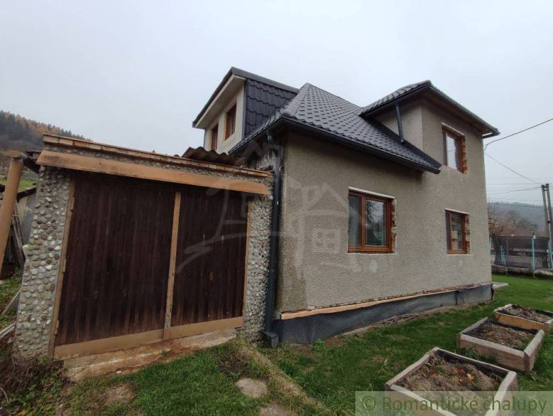 A family house in Jasenica with a wooden garage and garden planters on the lawn.