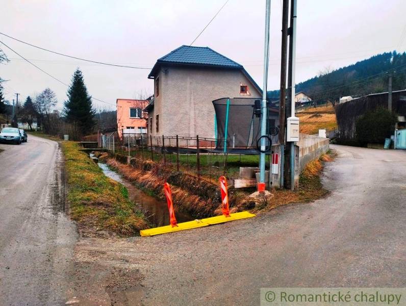 A family house in Jasenica by the road with a drainage channel and a fence.