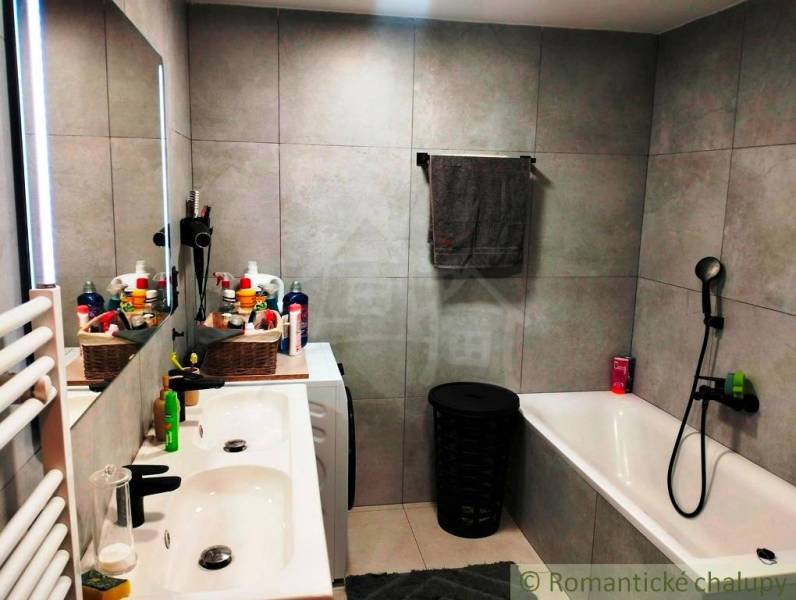 A bathroom in a family house with a bathtub, double sink, and light gray wall tiles.