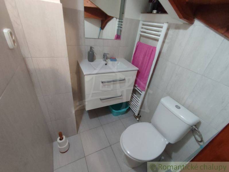 Bathroom in a family house with a sink, mirror, and toilet on light tiles.
