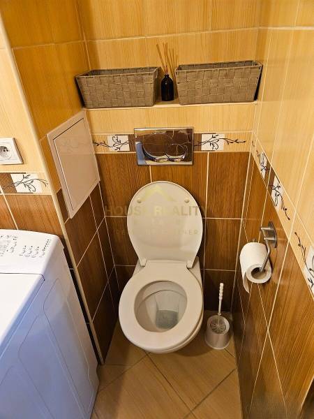 Toilet with tiles and a washing machine in a 3-room apartment, floor with wood decor.
